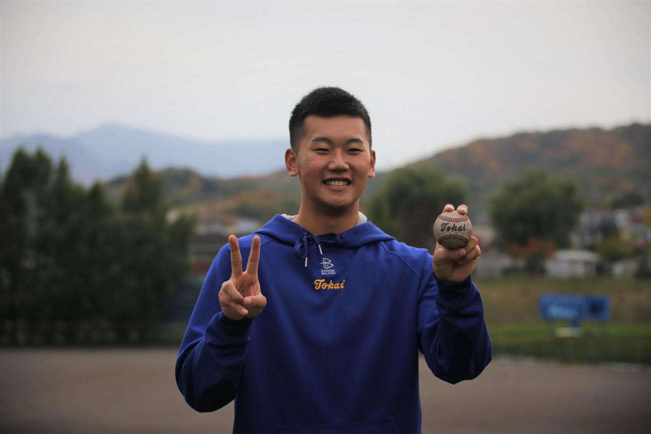 右手でドラフト2位のピースサイン、左手でボールを握って笑顔を見せる門別（撮影・中島洋尚）