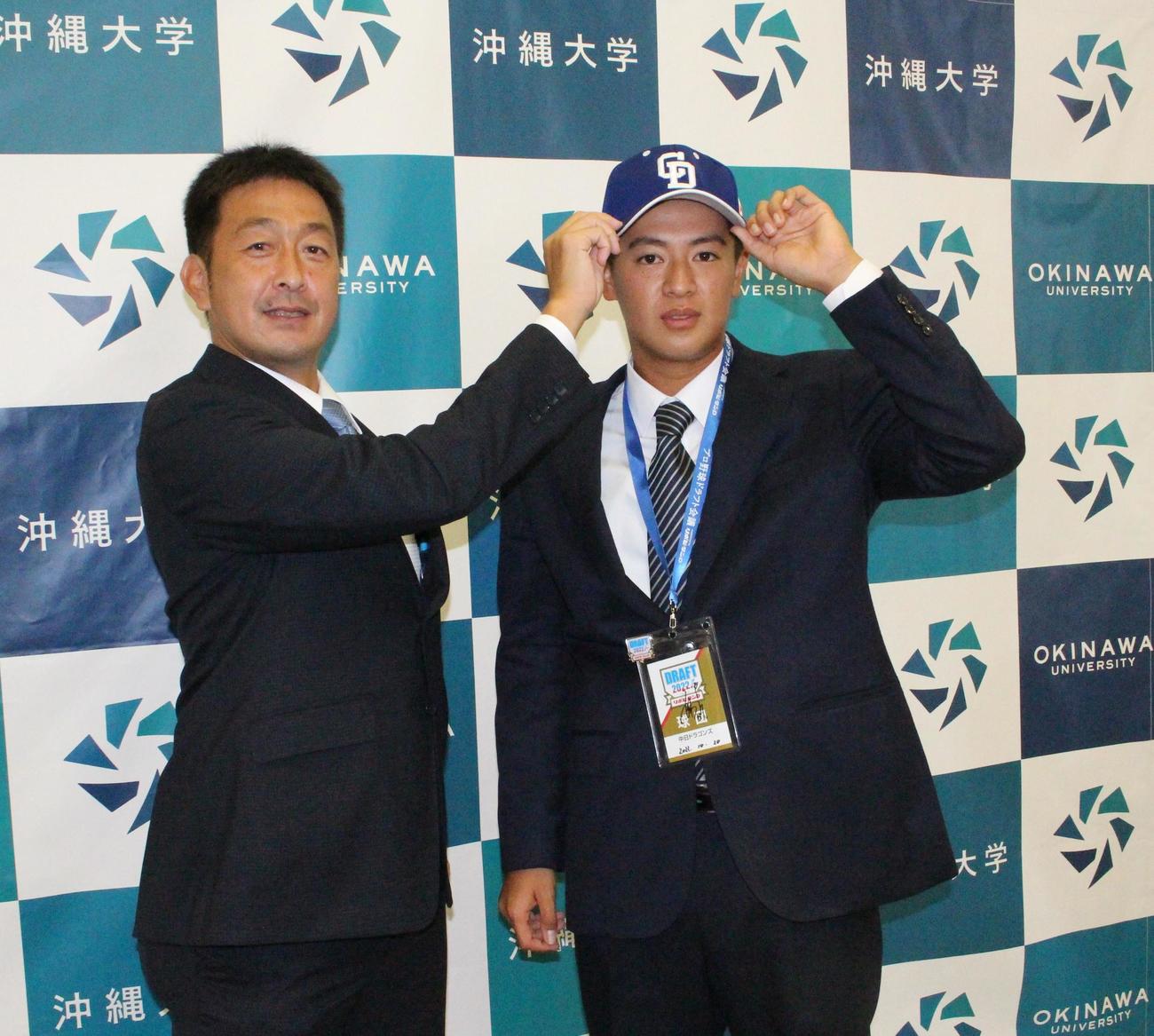中日の指名あいさつを受け、三瀬スカウトから帽子をかぶせてもらう沖縄大・仲地礼亜投手（撮影・菊川光一）