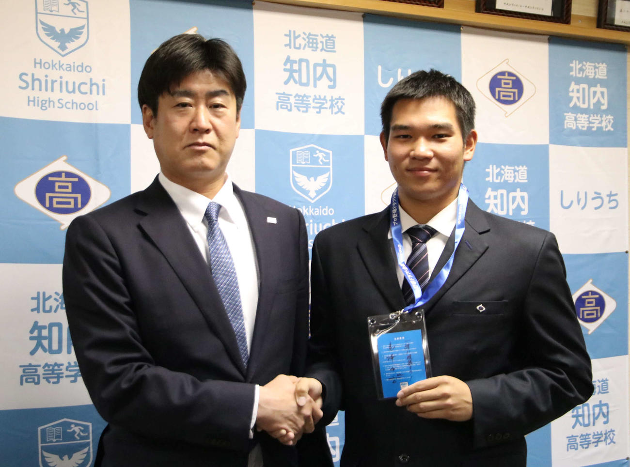 ヤクルトからドラフト4位指名を受けた知内・坂本（右）は高津監督のサインとメッセージが添えられたドラフト会議の入館証を手に斉藤スカウトと握手を交わす（撮影・山崎純一）