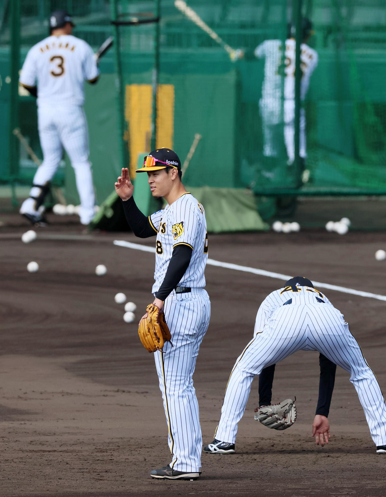 守備練習中、笑顔でナインにジェスチャーを送る佐藤輝。奥は打撃練習中の大山。右は高浜（撮影・加藤哉）