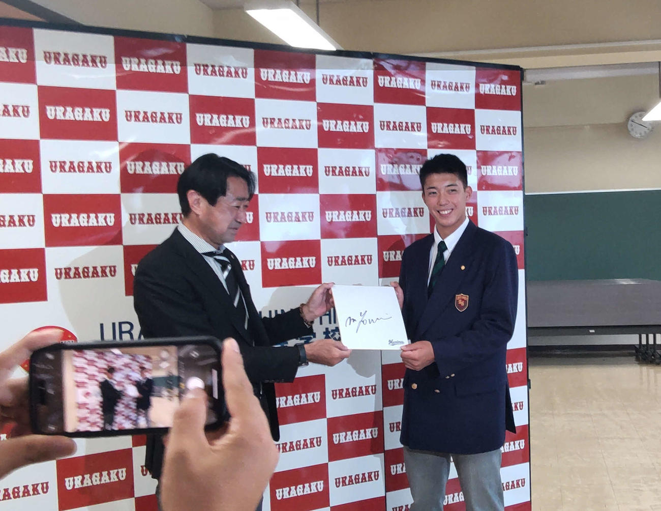 指名あいさつを受けたロッテのドラフト5位、浦和学院・金田優太内野手（右）は中川隆治スカウトらから吉井理人新監督のサイン色紙を渡され、にっこり
