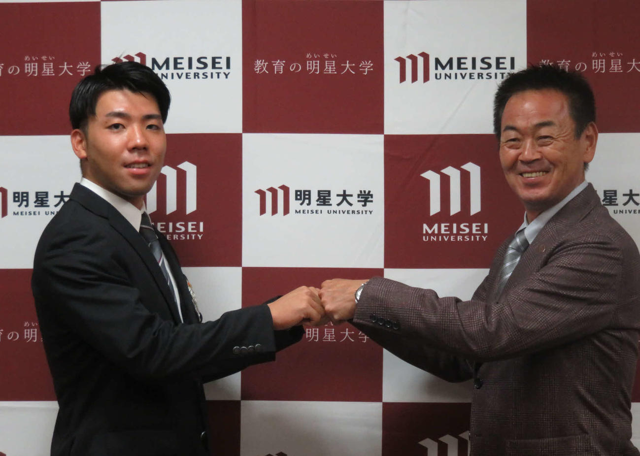 指名あいさつに訪れた巨人水野スカウト部長（右）と笑顔でグータッチする育成ドラフト1位の明星大・松井（撮影・小早川宗一郎）