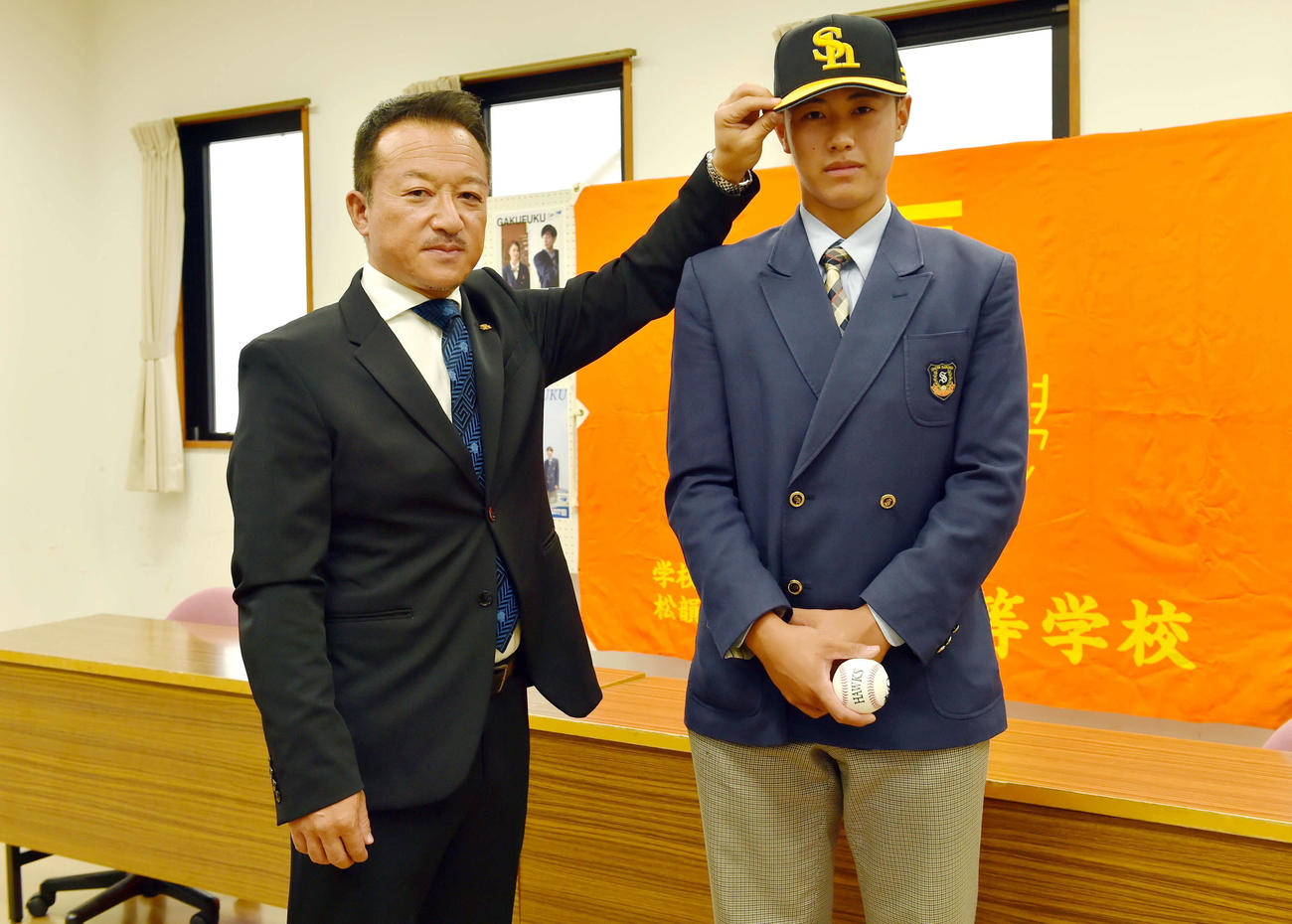 ソフトバンク作山アマスカウトチーフ補佐（左）に帽子をかぶらせてもらう学法福島・佐々木