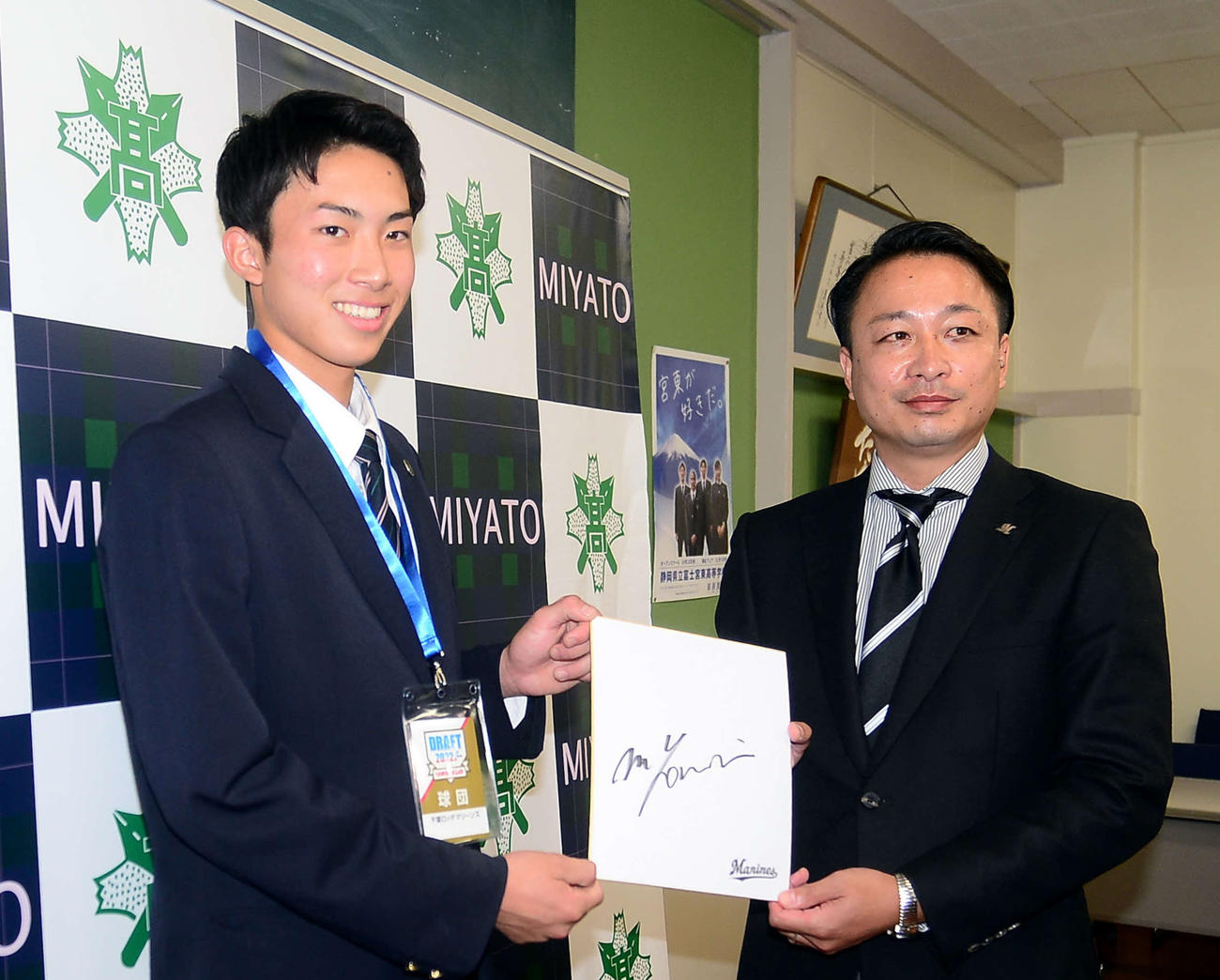 富士宮東・勝又（左）とロッテ小林担当スカウトは、吉井監督のサインを見せる