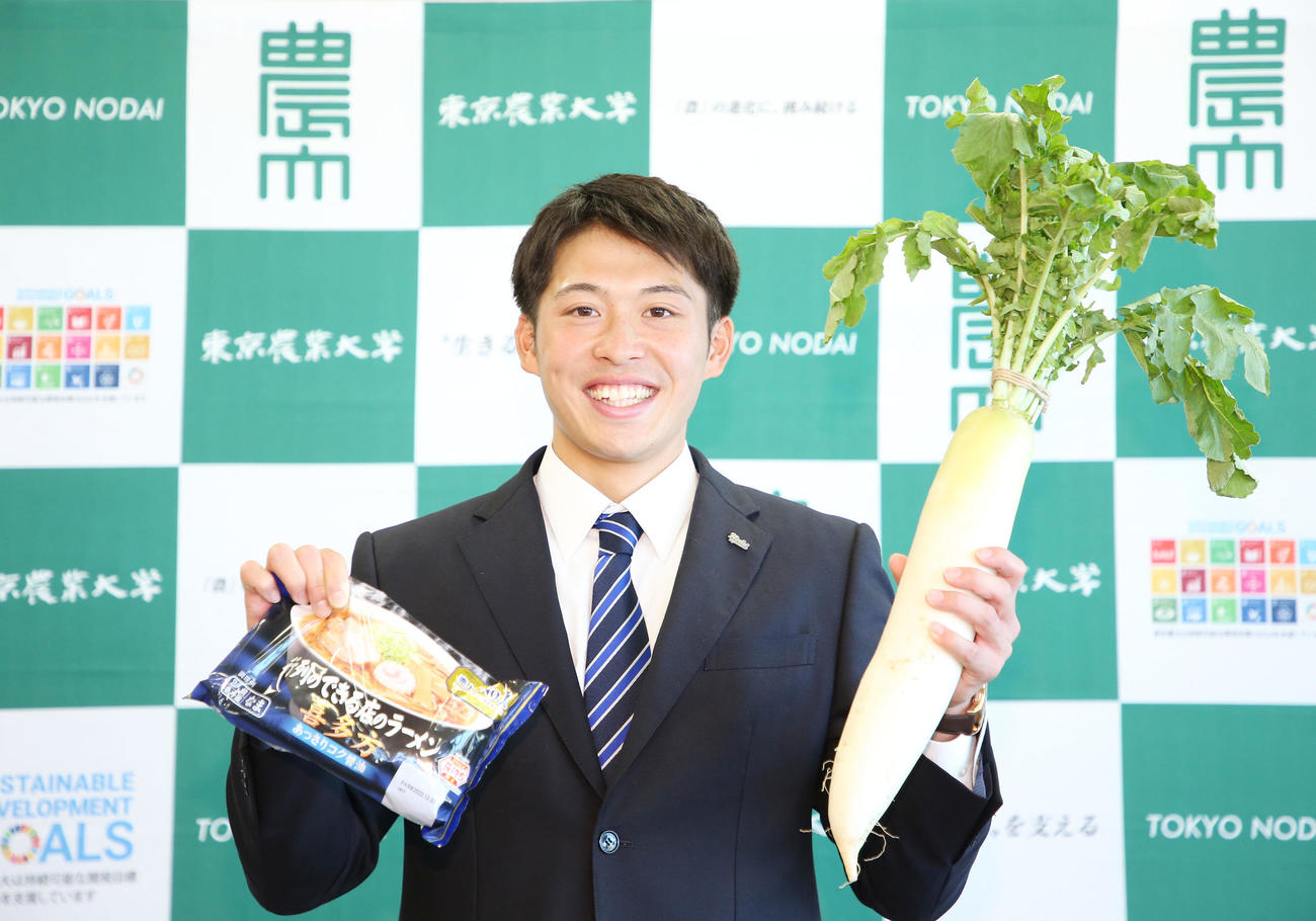 指名あいさつを受けた楽天ドラフト4位の東農大オホーツク・伊藤投手は喜多方ラーメンと大根を手に笑顔を見せる（撮影・宮地輝）