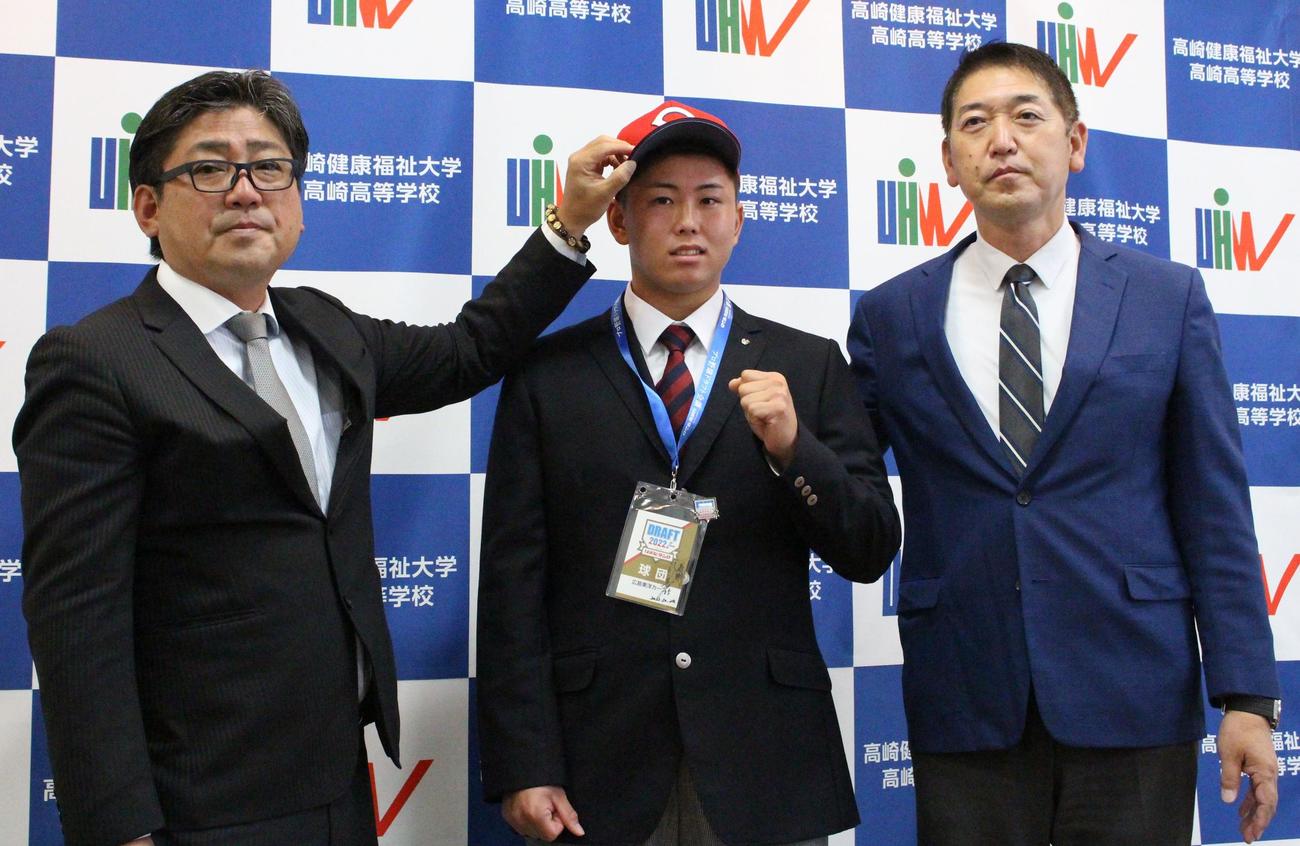 指名あいさつを受ける高崎健康福祉大高崎・清水（中央）と青柳監督（右）。帽子をかぶせる担当の広島・高山スカウト（左）（撮影・保坂恭子）