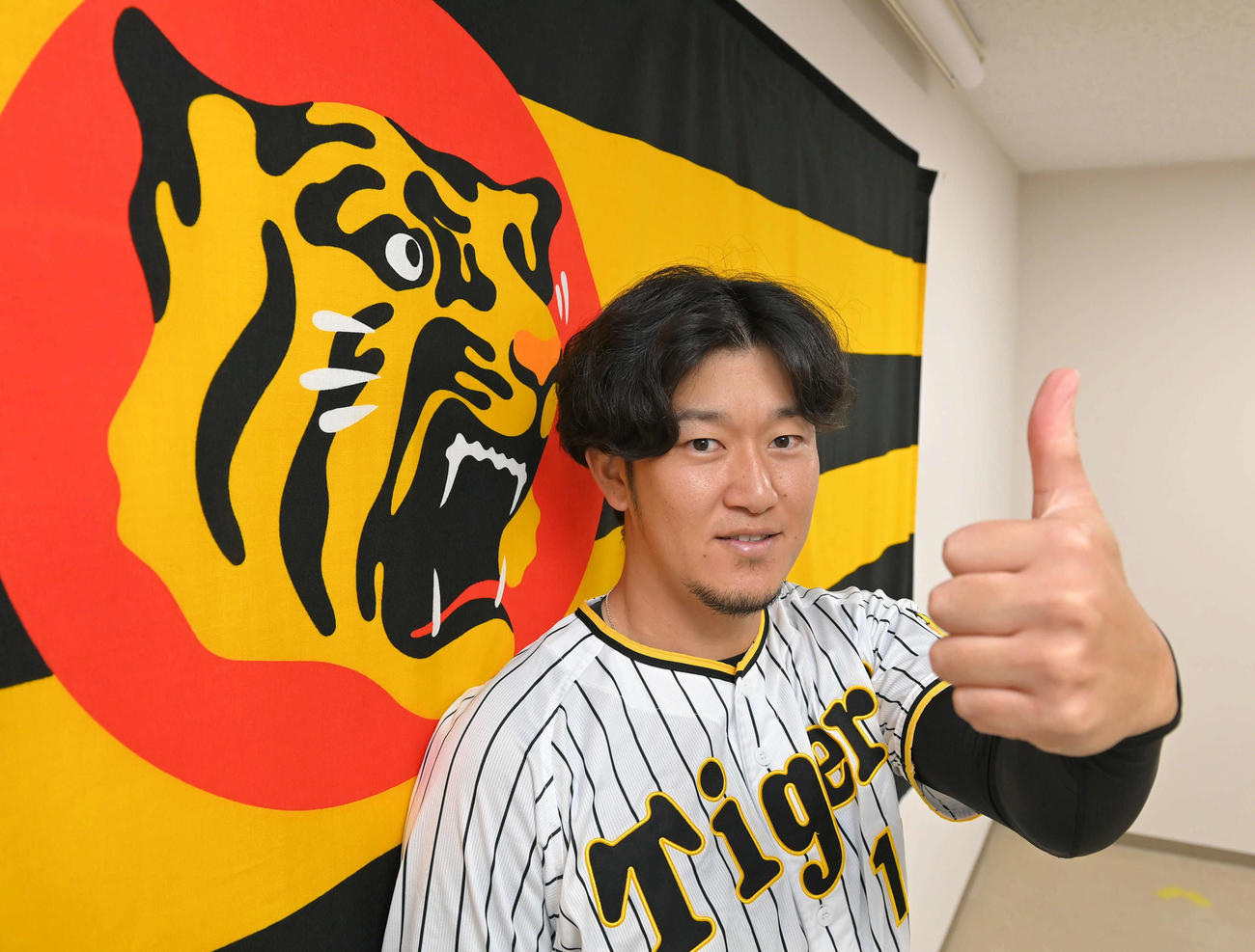 阪神残留を決め、虎マークを背にサムズアップポーズを決める岩貞（代表撮影）