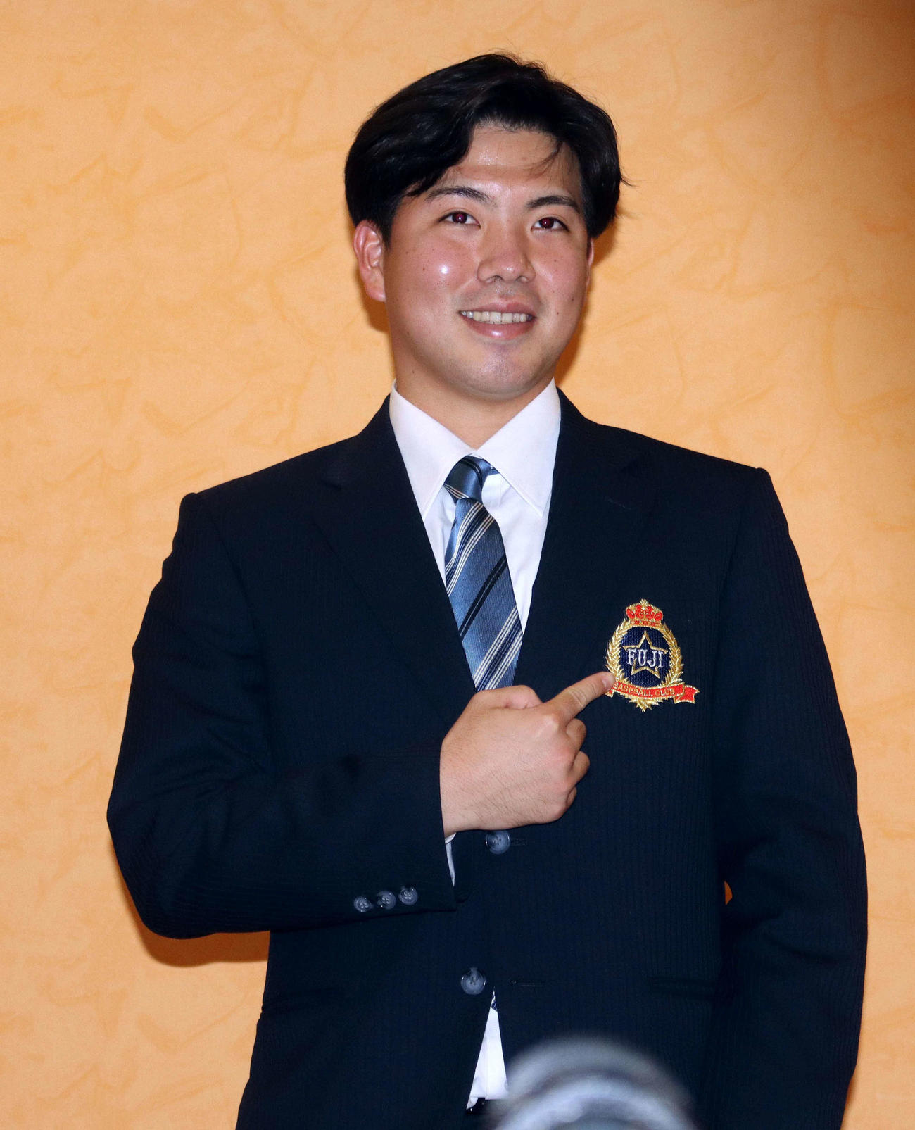 胸のエムブレムを指さす富士大・金村（撮影・永野高輔）