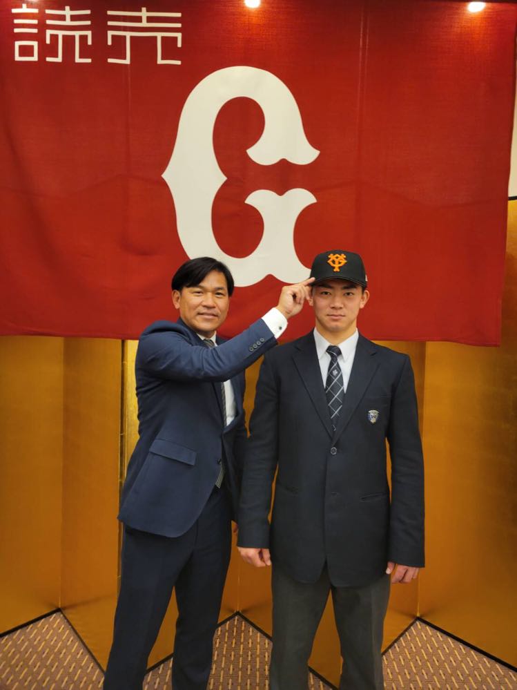仮契約を結び巨人の帽子を脇谷スカウトからかぶせてもらう育成5位の相沢（球団提供）