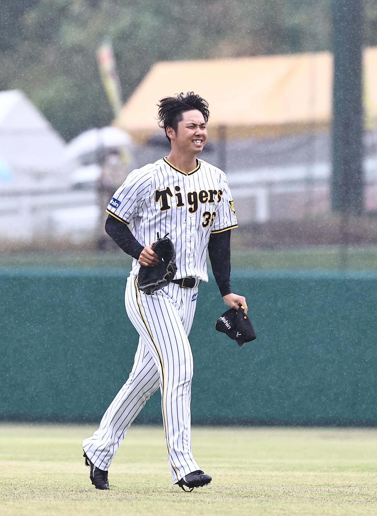 大雨が降る中、傘もささずにサブグラウンドを移動する阪神浜地（撮影・上田博志）