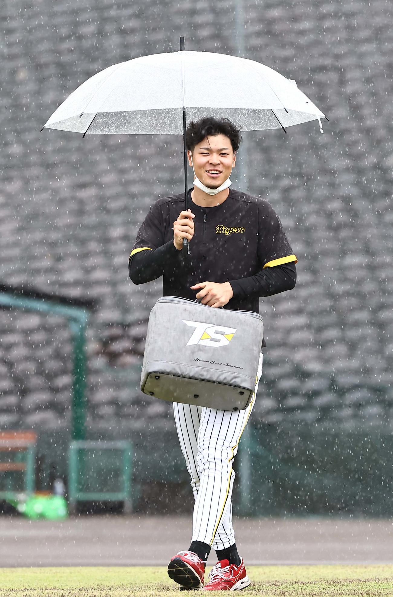 大雨の中、傘をさしながら安芸ドームへ向かう佐藤輝（撮影・上田博志）