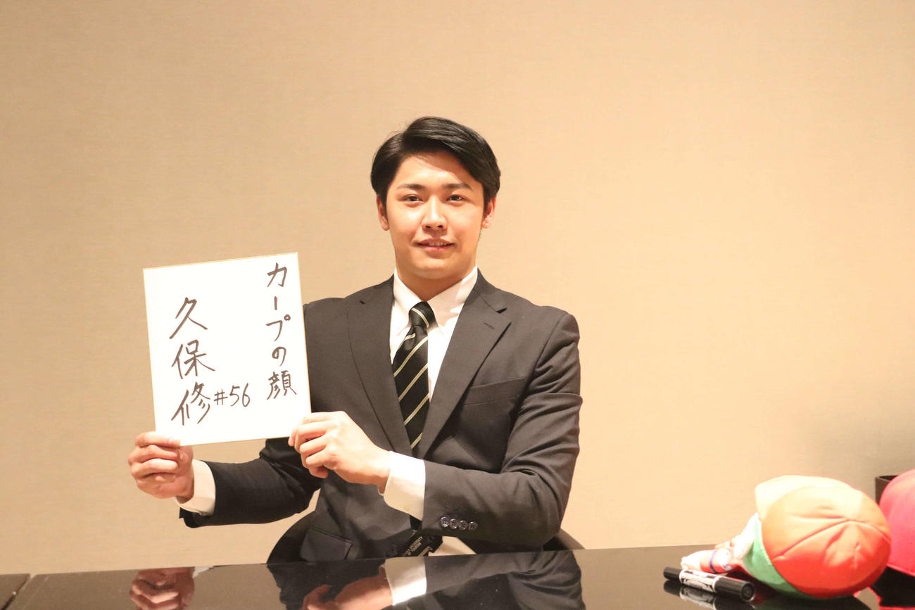 仮契約を行った、色紙を掲げる広島ドラフト7位の大阪観光大・久保修外野手