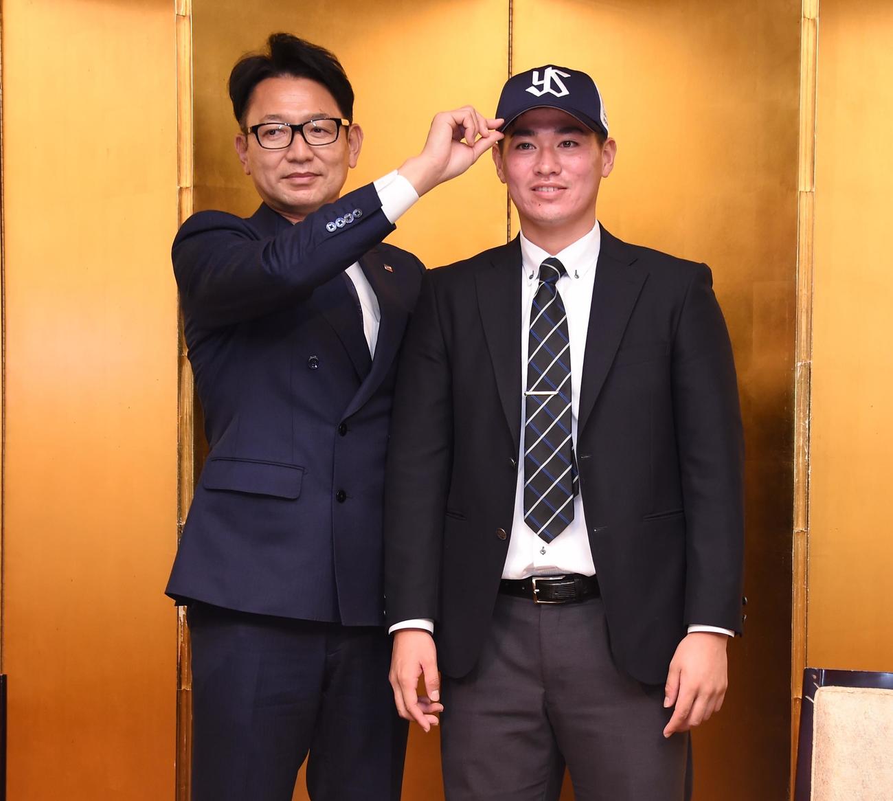 ヤクルトからドラフト5位指名を受けた中大・北村（右）は仮契約を終え、橿渕スカウトデスクから帽子をかぶせてもらう（撮影・鈴木正章）