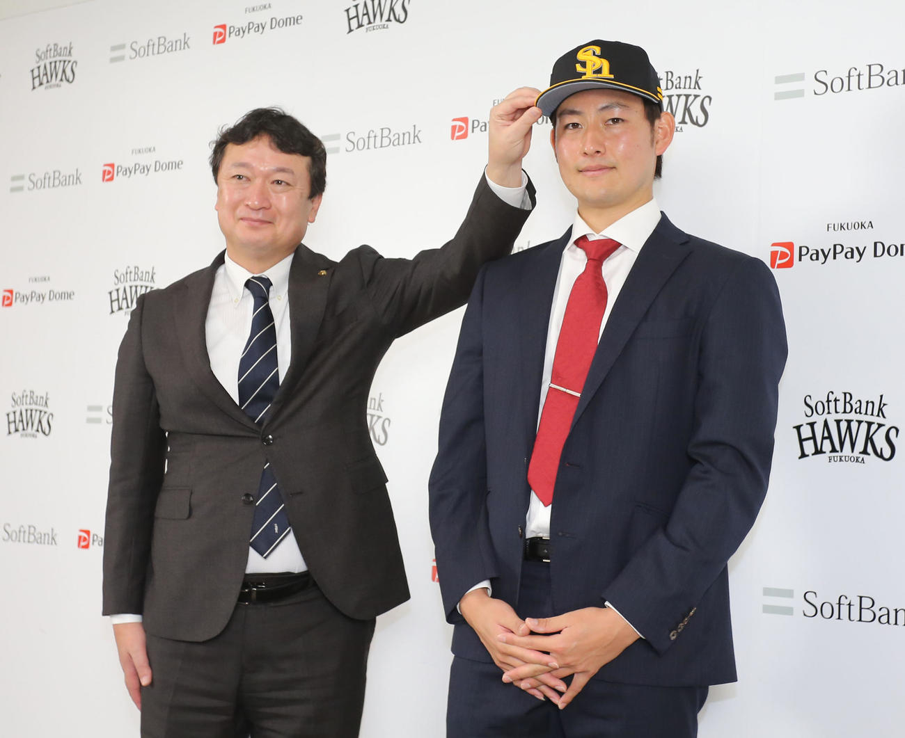 入団会見で三笠取締役GM（左）から帽子をかぶせてもらう渡辺（撮影・屋方直哉）