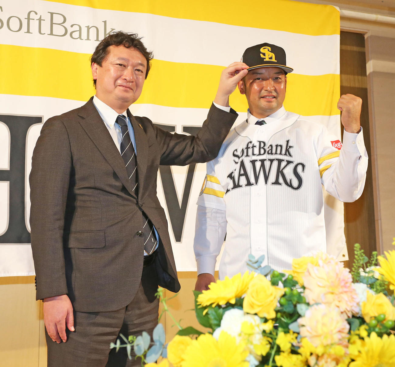 入団会見でユニホームに袖を通す嶺井。左は三笠取締役GM（撮影・屋方直哉）