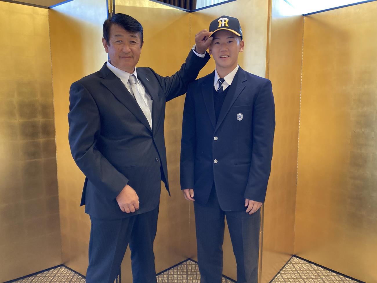 阪神と仮契約を結んだ東海大札幌・門別（右）は葛西稔スカウトに帽子をかぶせてもらう（阪神タイガース提供）