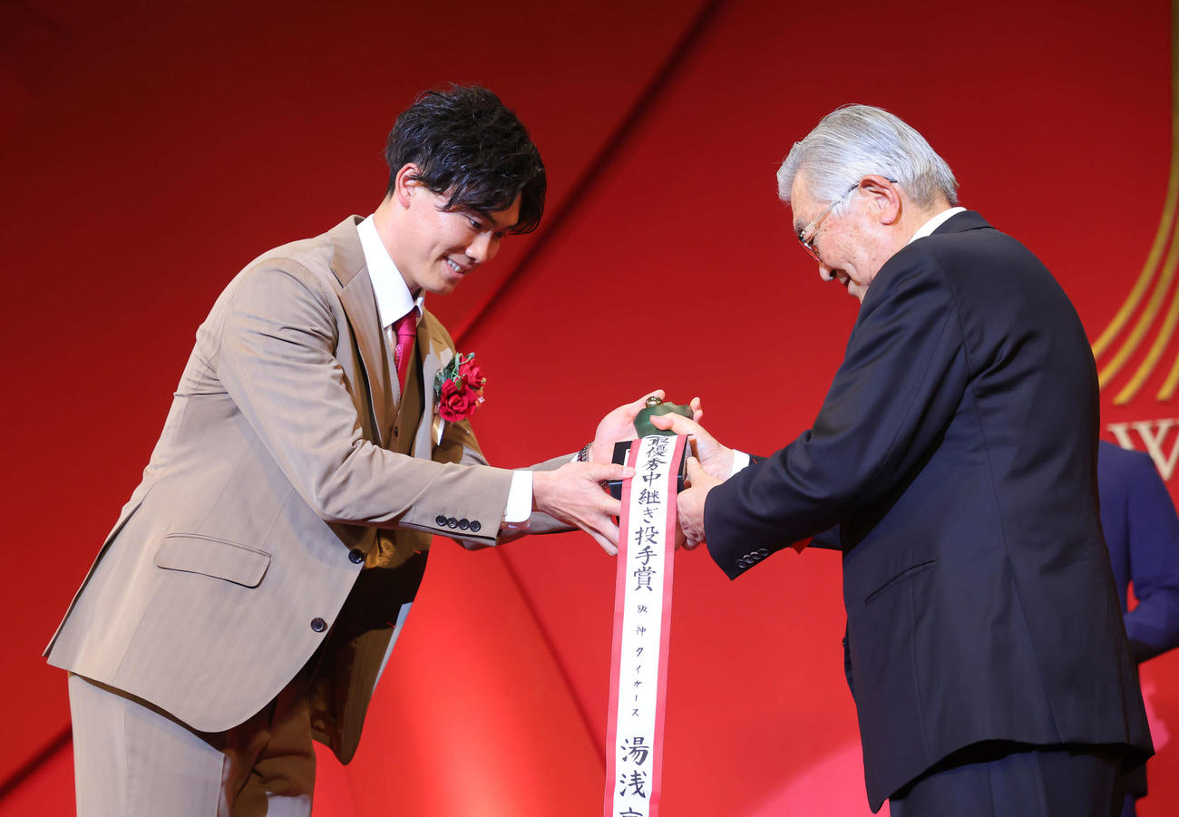 「NPB AWARDS 2022」でセ・リーグ最優秀中継ぎ投手賞に輝いた阪神湯浅（左）は斉藤コミッショナーから笑顔でトロフィーを受け取る（代表撮影）