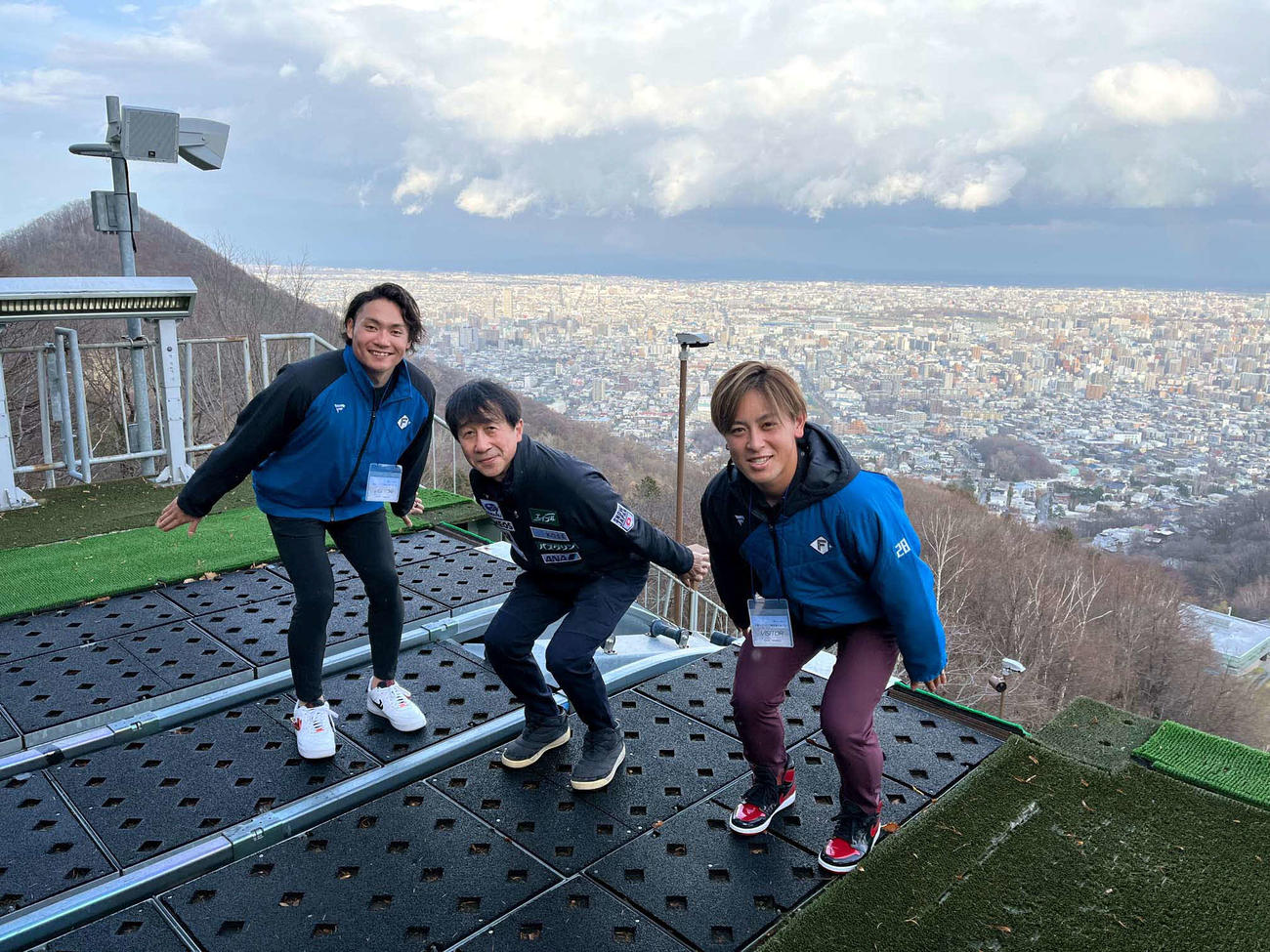 大倉山ジャンプ競技場のスタート地点で、札幌の町並みをバックに滑走ポーズをする（左から）日本ハム伊藤、原田氏、日本ハム河野（撮影・永野高輔）