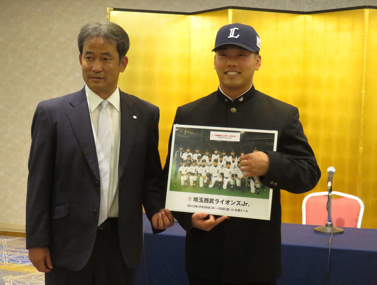 契約交渉を終え、ライオンズジュニア時代の写真に笑顔のドラフト1位・早大蛭間（右）と潮崎編成ディレクター