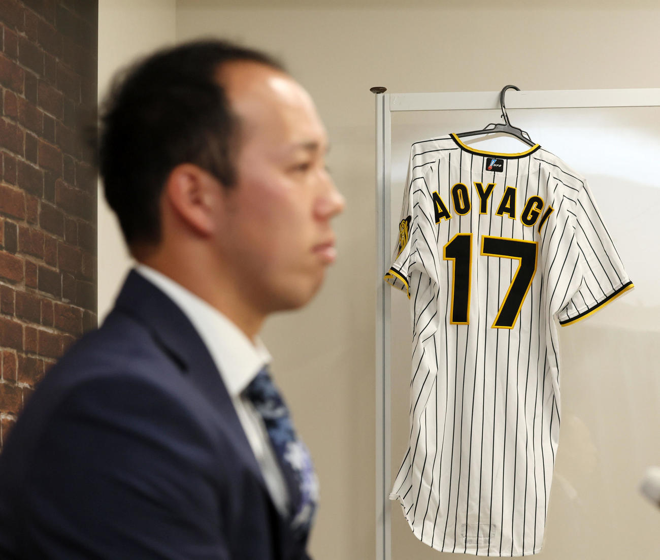 新背番号「17」番のユニホームを横目に契約更改の会見をする青柳（撮影・加藤哉）