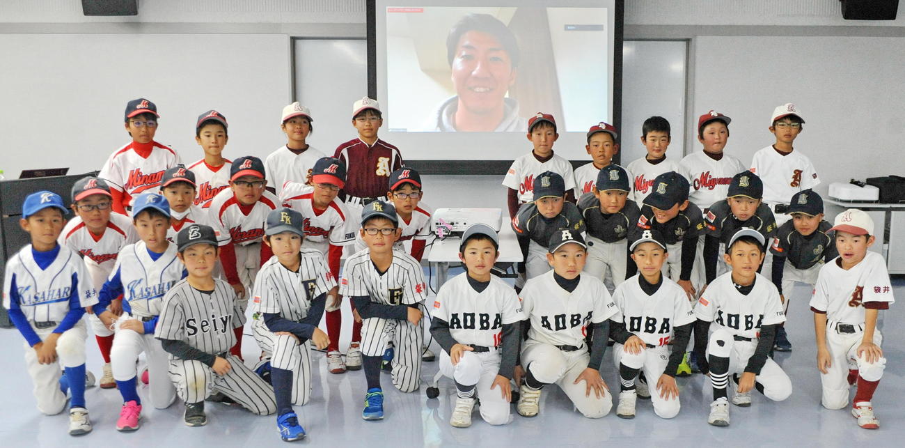 スクリーンに映る浦野氏と記念撮影に納まる袋井市少年野球チームの選手たち　