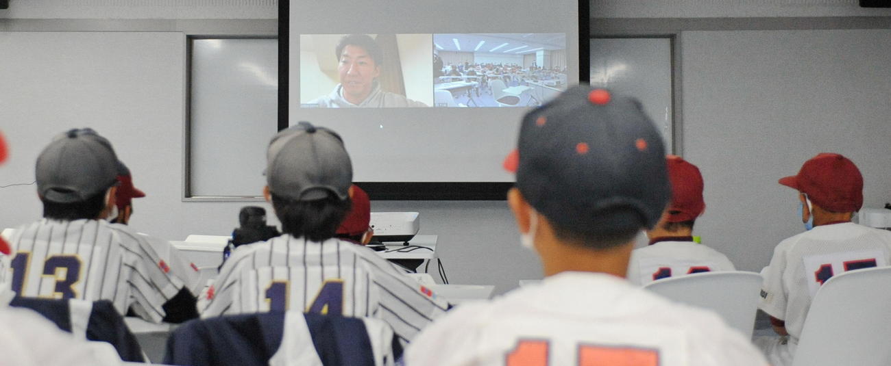 スクリーンに映る浦野氏の話を聞く選手たち