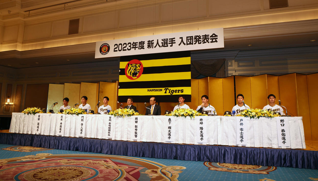 新人選手入団発表会見で壇上に座るナインと岡田監督（左から5人目）、同4人目は百北球団社長（撮影・加藤哉）