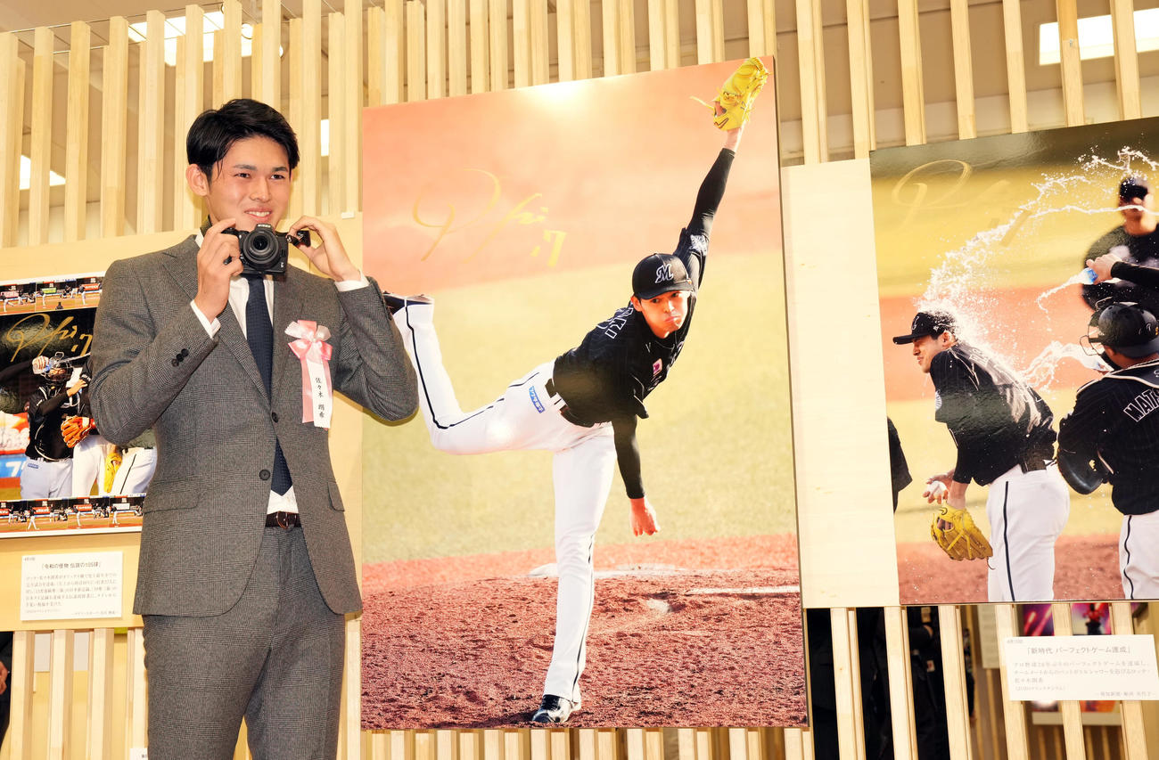 日本橋三越で行われる第63回2022年報道写真展で、自身の完全試合達成時の写真を前に、カメラを手に笑顔を見せるロッテ佐々木朗（撮影・狩俣裕三）