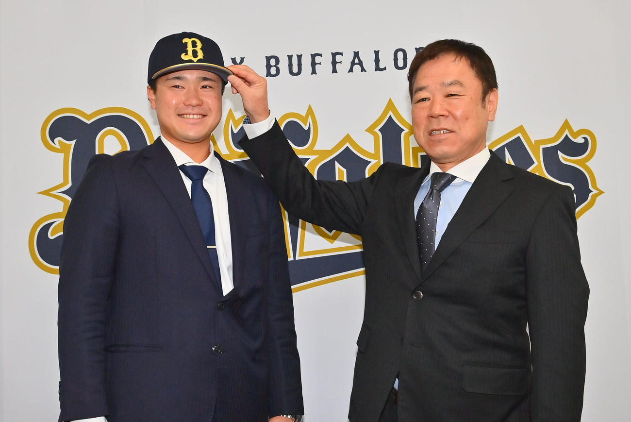 現役ドラフトでオリックスに入団し、福良GM（右）から帽子をかぶせてもらう渡辺（撮影・和賀正仁）