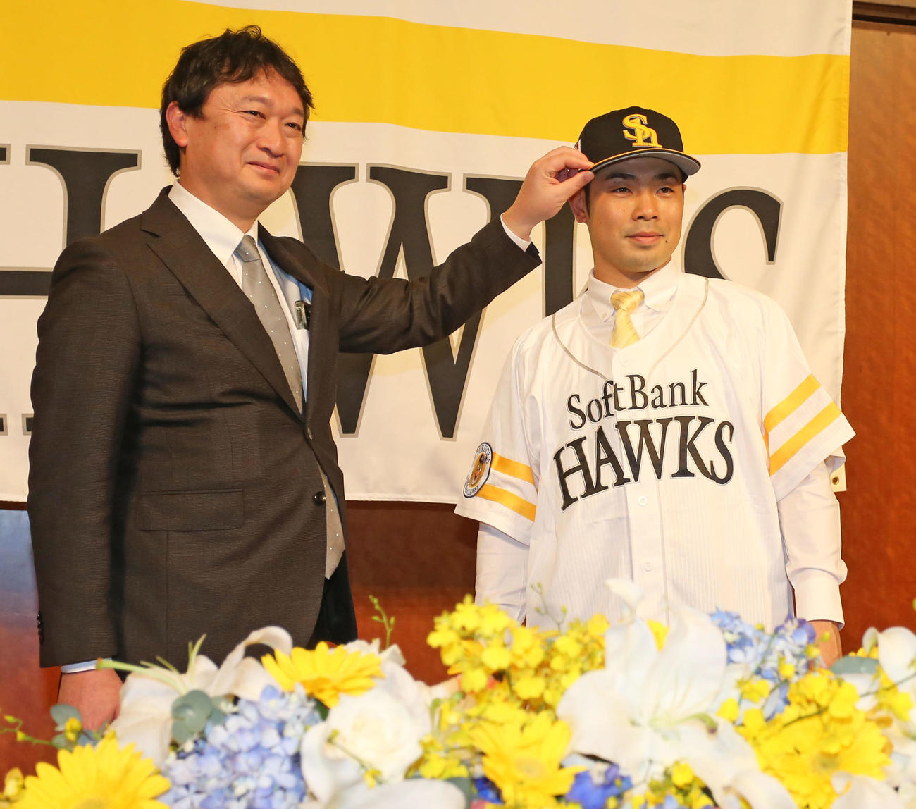 入団会見でユニホームに袖を通す近藤。左は三笠取締役GM（撮影・屋方直哉）