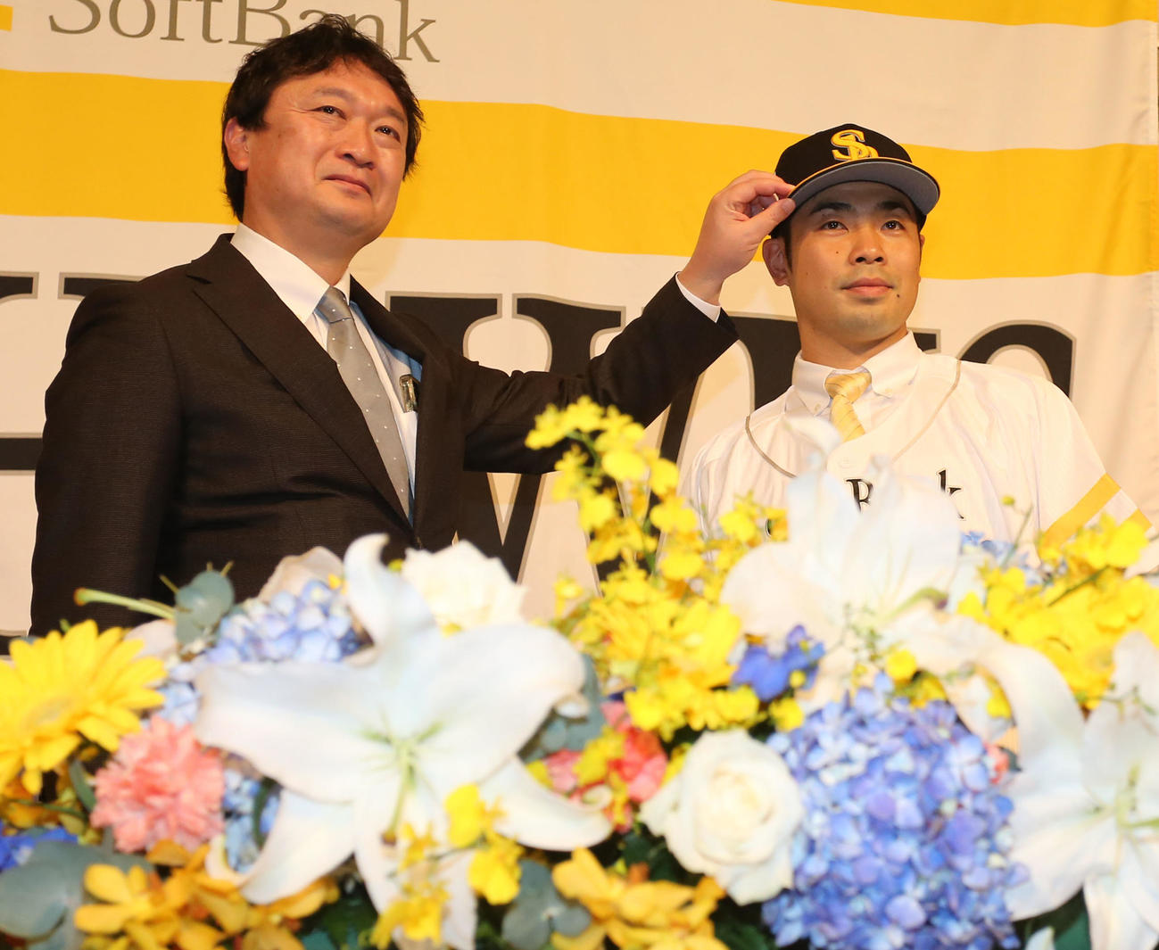 入団会見でユニホームに袖を通す近藤。左は三笠取締役GM（撮影・屋方直哉）