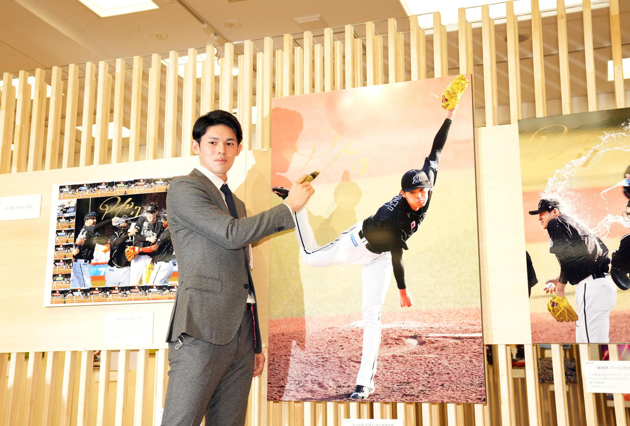 日本橋三越で行われる第63回2022年報道写真展のオープニングで完全試合達成時の写真にサインをするロッテ佐々木朗（撮影・狩俣裕三）