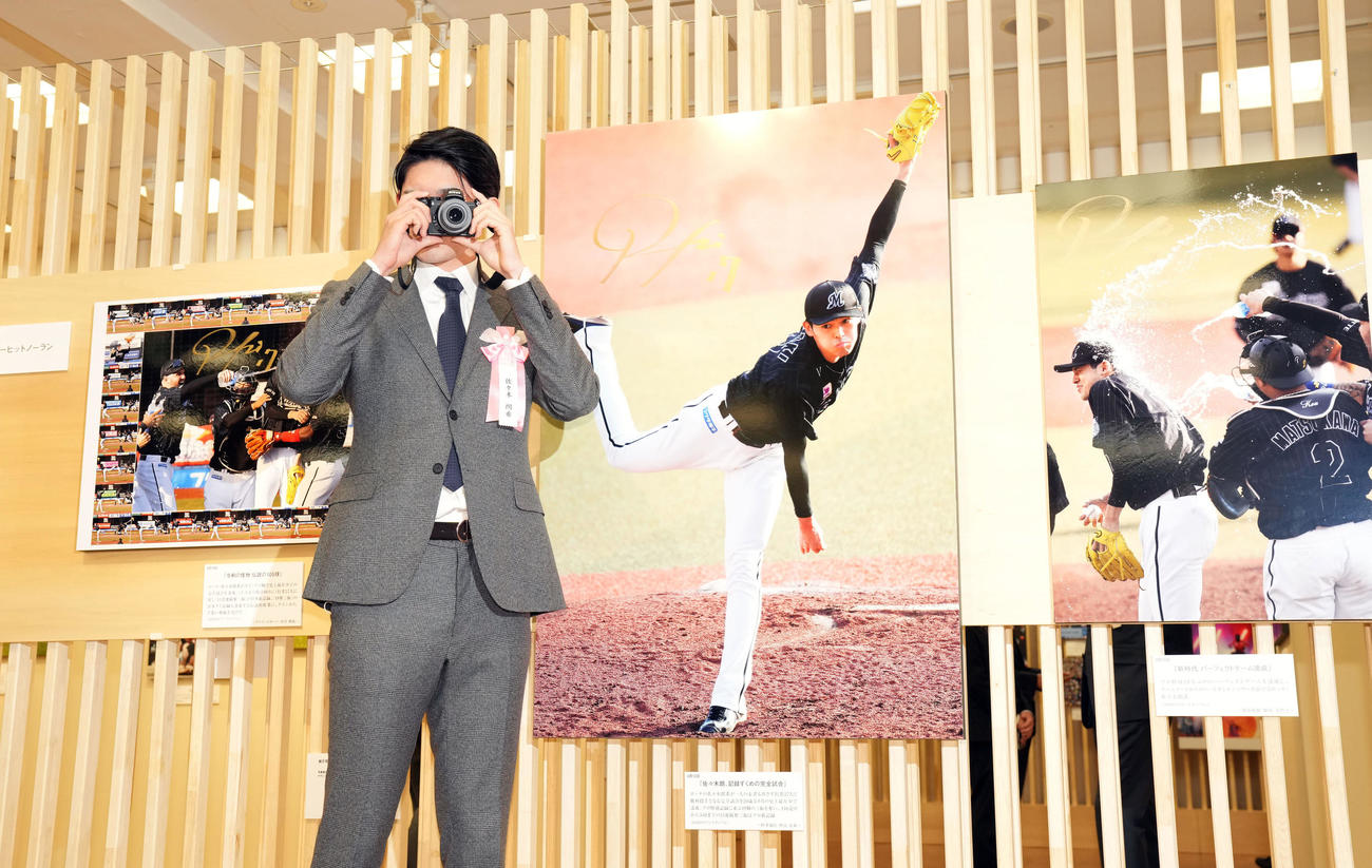 日本橋三越で行われる第63回2022年報道写真展のオープニングで完全試合達成時の写真を前に、カメラで報道陣を撮影するロッテ佐々木朗（撮影・狩俣裕三）