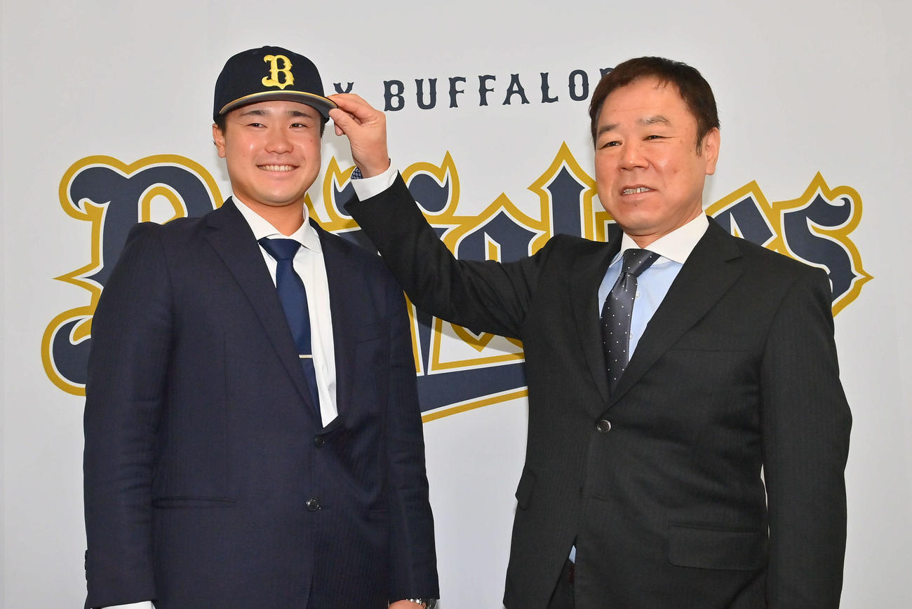 現役ドラフトでオリックスに入団し、福良GM（右）から帽子をかぶせてもらう渡辺（撮影・和賀正仁）