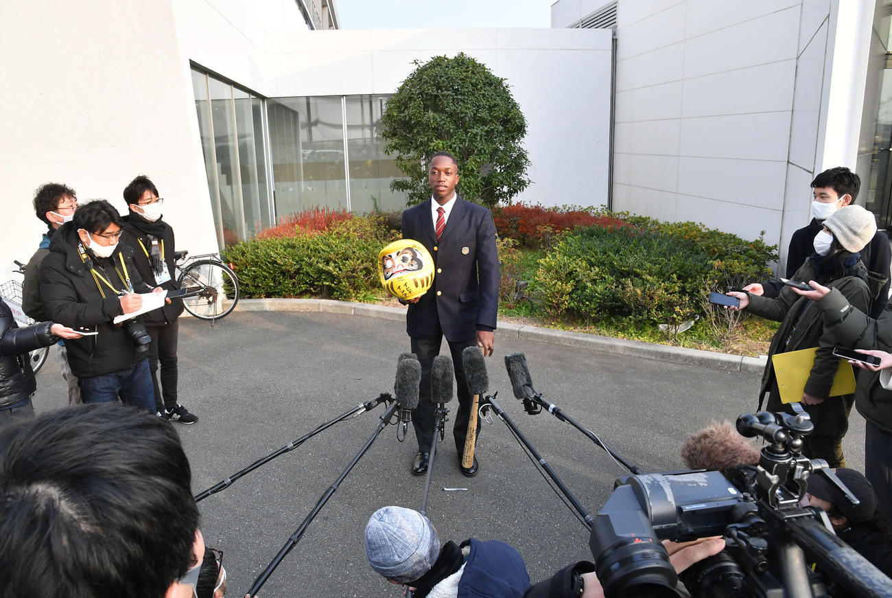 若鷹寮へ到着し、小学校の頃に所属していた少年野球チームから贈られた黄色いだるまとバットを手に囲み取材を受けるドラフト1位のイヒネ（撮影・岩下翔太）