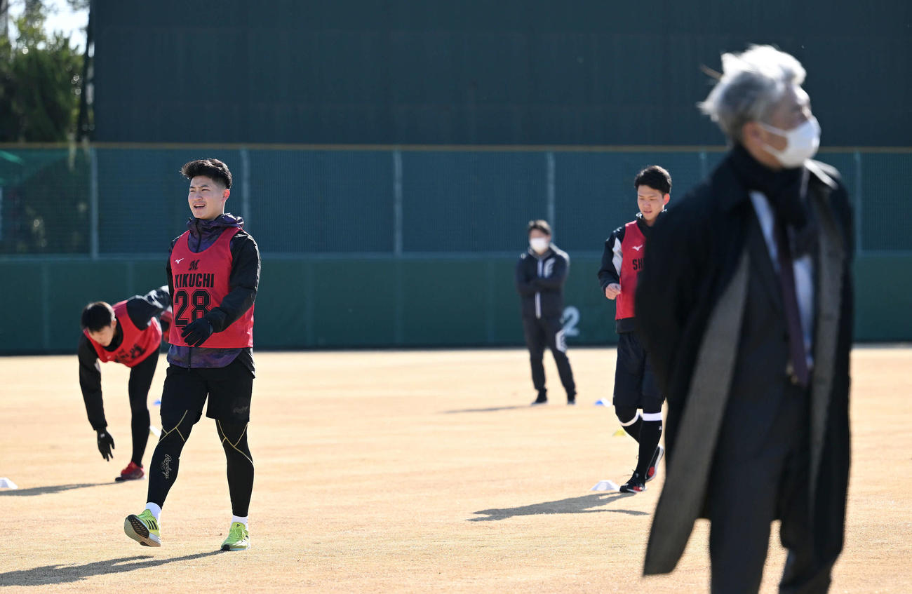 ロッテ新人合同自主トレの視察に訪れた吉井監督（手前右）の奥でウオーミングアップするドラフト1位の専大・菊地（左から2人目）ら（撮影・滝沢徹郎）