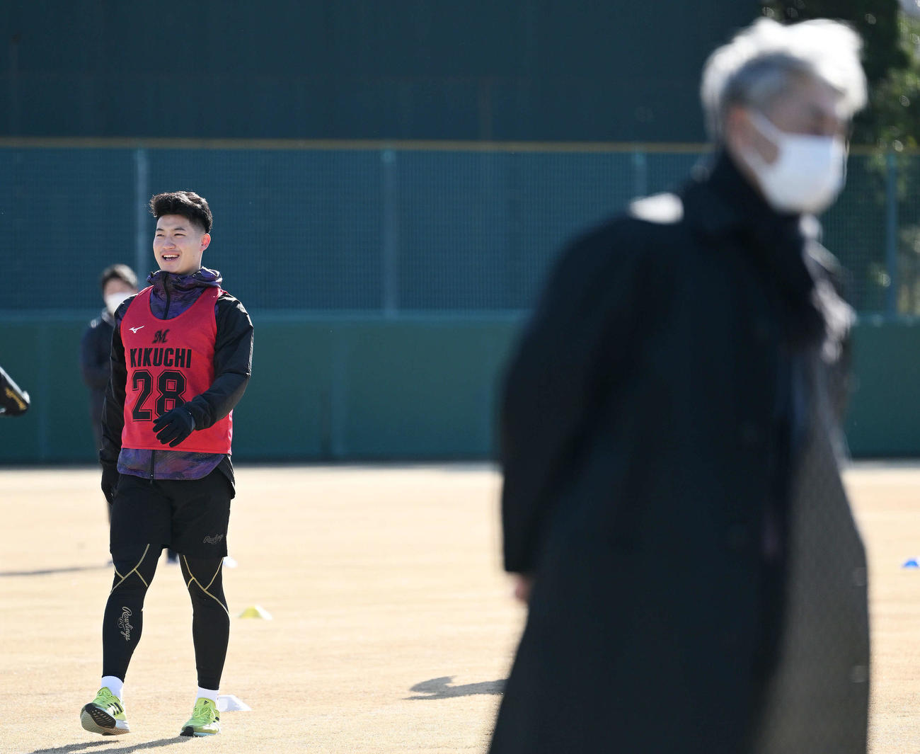ロッテ新人合同自主トレの視察に訪れた吉井監督の奥でウオーミングアップするドラフト1位の専大・菊地（撮影・滝沢徹郎）