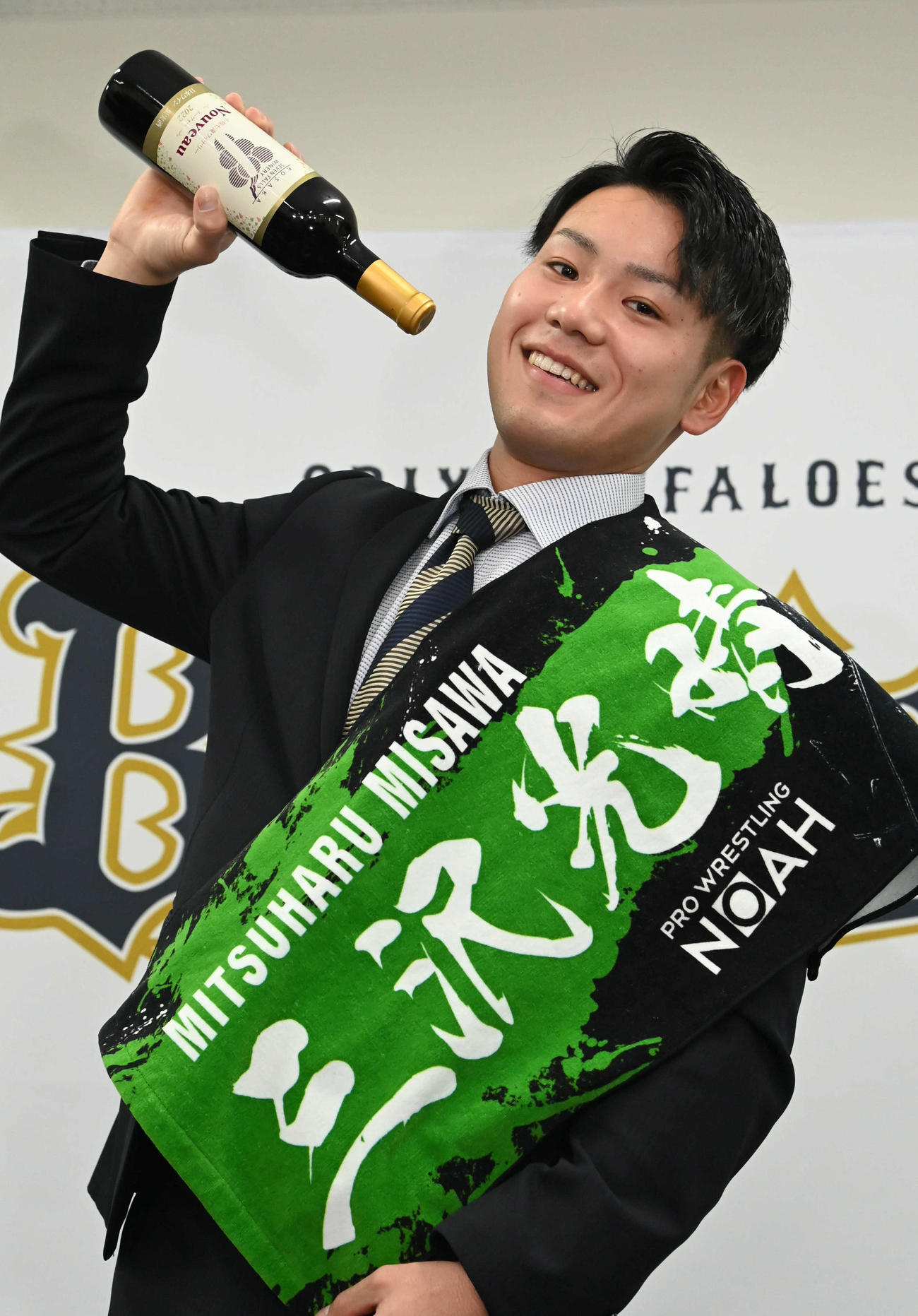 三沢光晴のタオルを肩にかけ、地元市長から贈られたワインを飲むポーズをするオリックス杉沢（撮影・石井愛子）