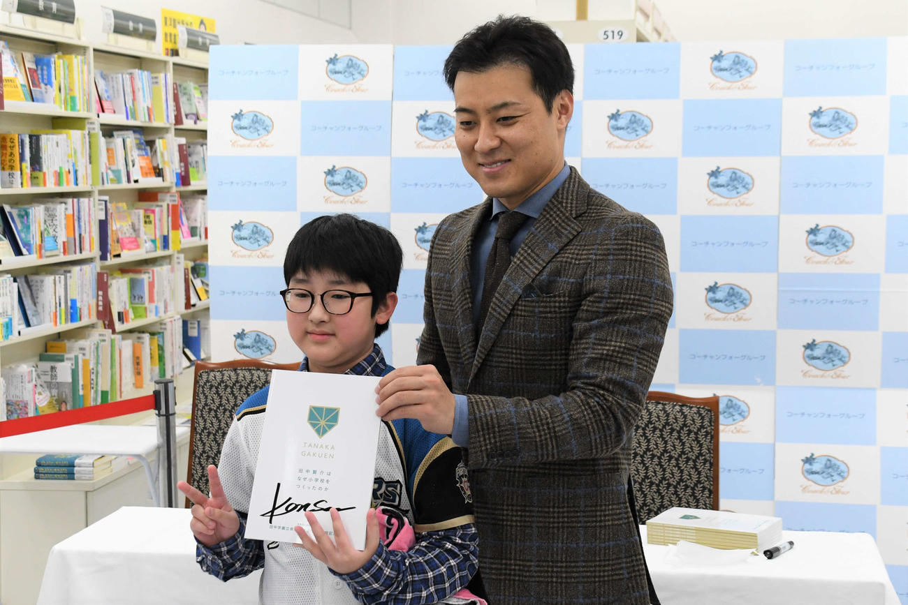 サイン入りの書籍を手に来場者と記念撮影する田中SA（右）（撮影・石井翔太）