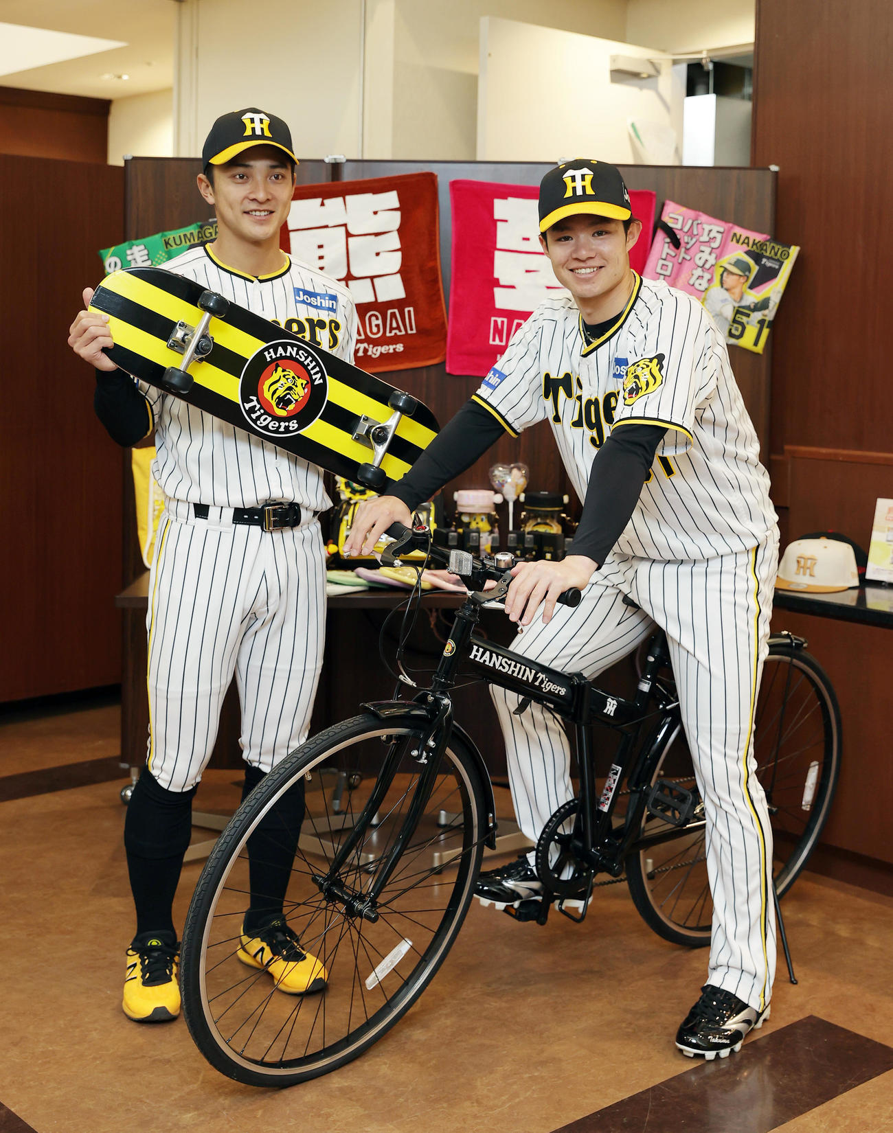 新作グッズのスケボーを手に笑顔を見せる阪神熊谷（左）とクロスバイクにまたがり笑顔を見せる中野（撮影・前田充）