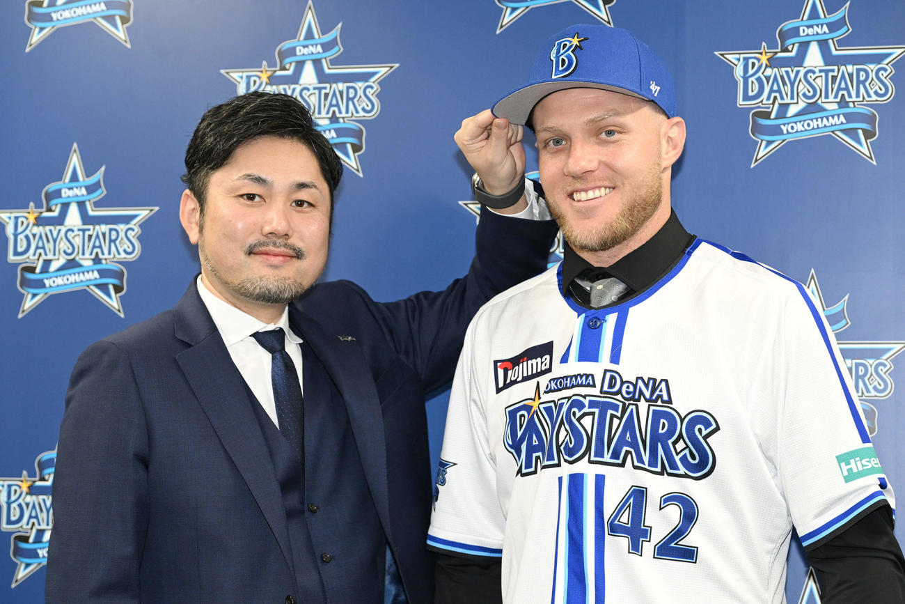 DeNA新外国人入団会見でアンバギー（右）は萩原チーム統括本部長から帽子をかぶらせてもらう（撮影・滝沢徹郎）