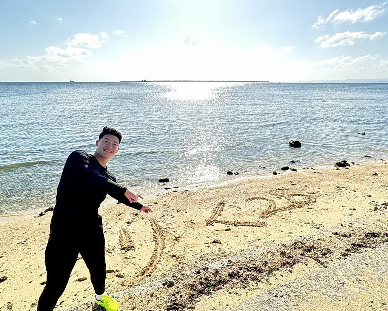 宿舎近くの砂浜に名前と背番号を記して笑顔を見せるロッテ菊地（球団提供）