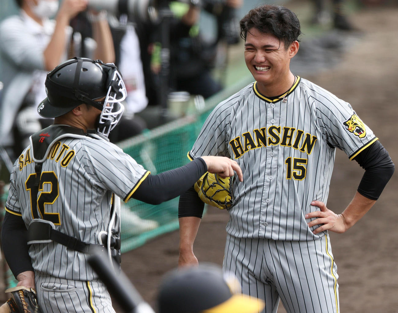シート打撃で1回目の登板を終えた西純矢（右）はベンチ前で坂本誠志郎の話を聞きながら笑顔を見せる（撮影・上山淳一）