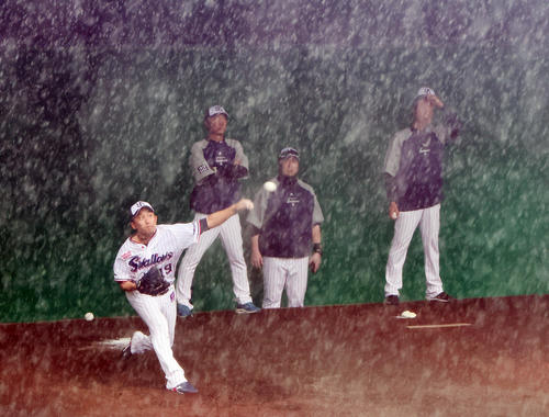 土砂降りの雨の中、ブルペンで投球練習するヤクルト石川（左端）。すぐ後ろで見つめる高津監督（左から2人目）の顔も雨で隠れてしまいそうです（撮影・足立雅史）