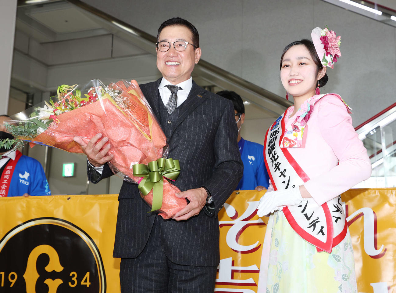 那覇空港での歓迎セレモニーで、那覇観光キャンペーンレディ（右）から花束を受け取り笑顔の巨人原監督（撮影・宮地輝）