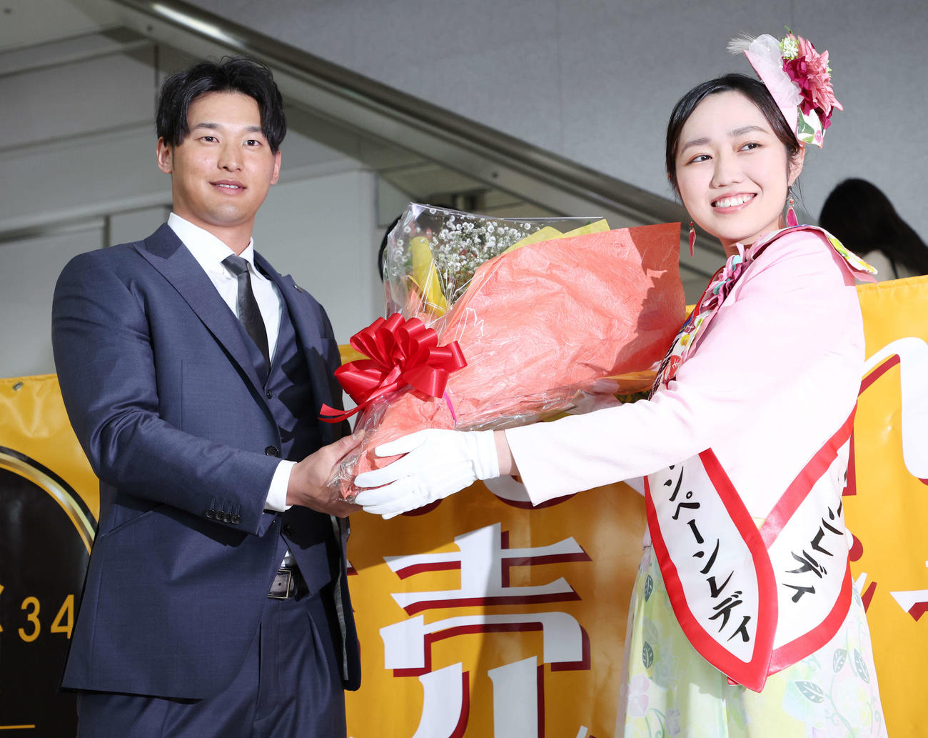 那覇空港での歓迎セレモニーで、那覇観光キャンペーンレディ（右）から花束を受け取り笑顔の巨人吉川（撮影・宮地輝）