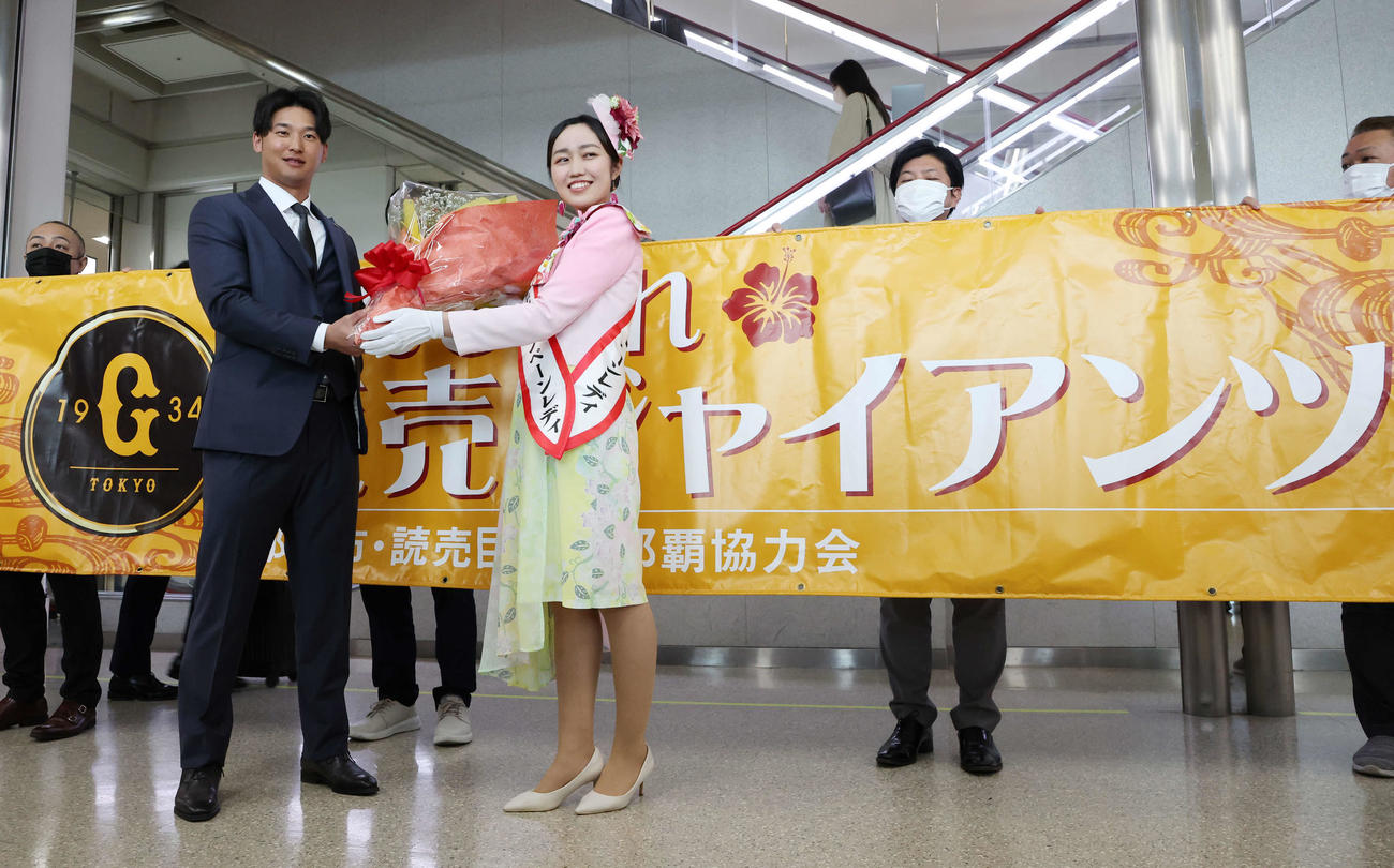 那覇空港での歓迎セレモニーで、那覇観光キャンペーンレディ（右）から花束を受け取り笑顔の巨人吉川（撮影・宮地輝）