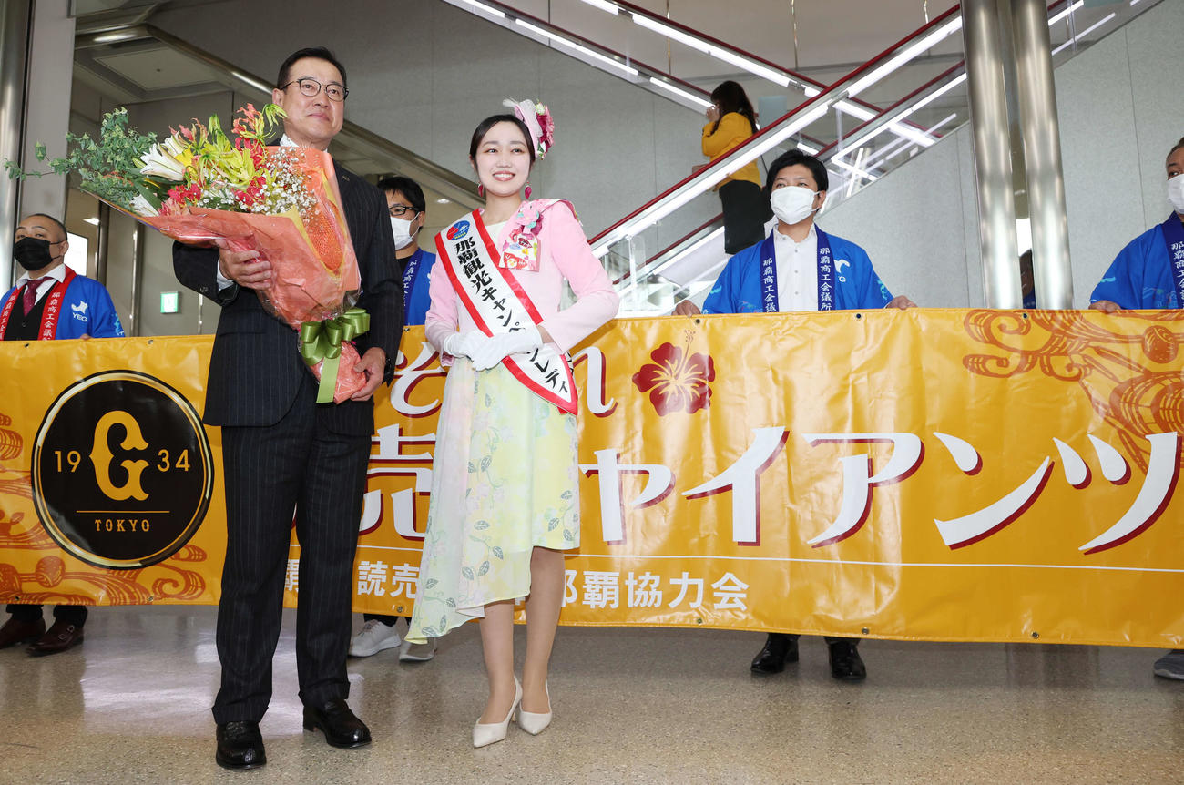 那覇空港での歓迎セレモニーで、那覇観光キャンペーンレディ（右）から花束を受け取り笑顔の巨人原監督（撮影・宮地輝）
