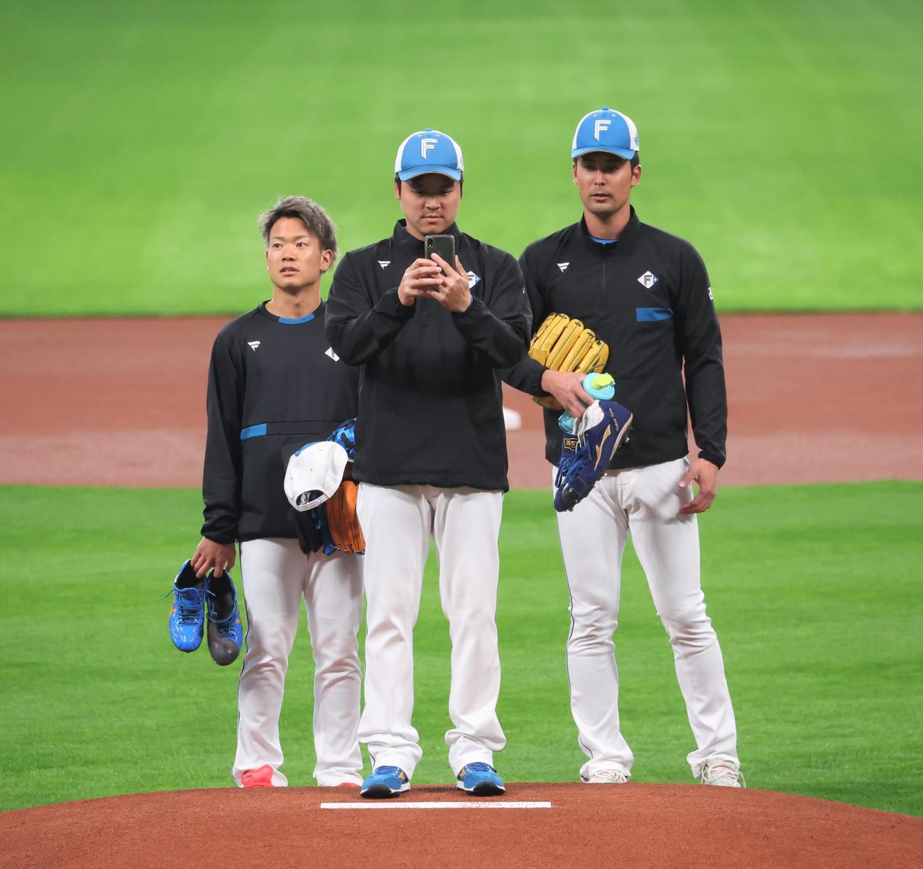 新球場エスコンフィールド北海道のマウンドからスマートフォンで撮影する日本ハム金村（中央）（撮影・黒川智章）