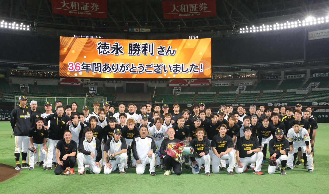36年間グラウンドを整えた徳永グラウンドキーパーと集合写真に納まるホークスナイン（撮影・冨田成美）
